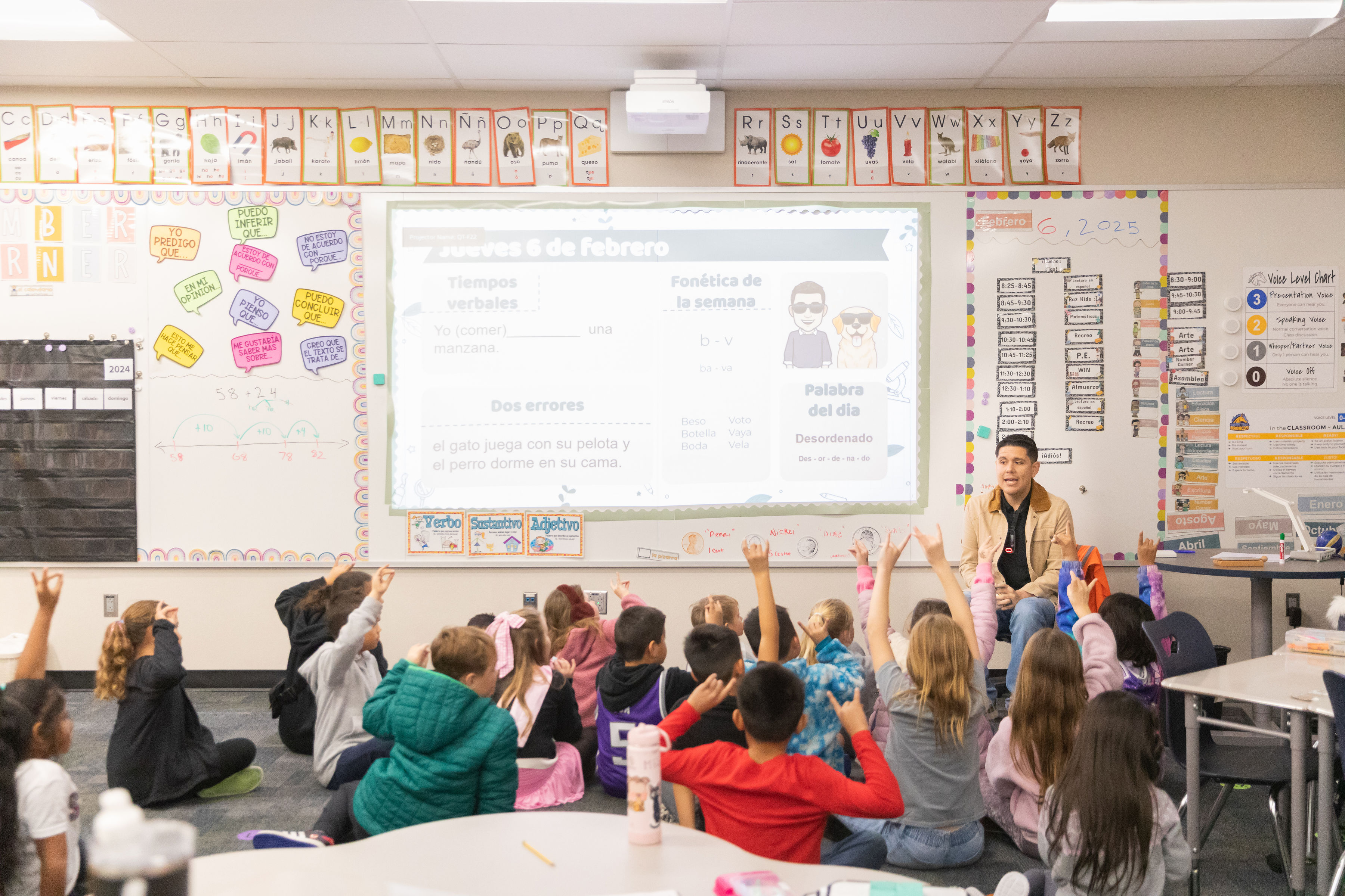 Quarry Trail Spanish Dual Language teacher sitting in front of his students with some raising their hands.